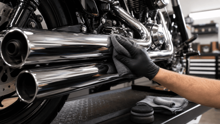 Chrome motorcycle exhaust being polished with microfiber cloth in a garage